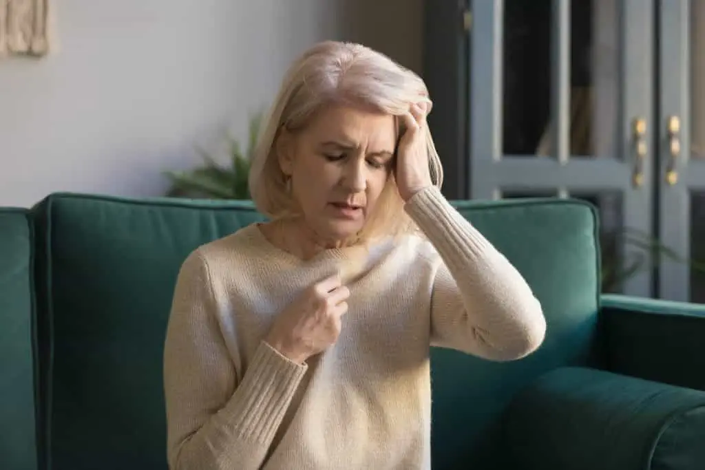 Eine Frau sitzt mit der Hand auf dem Kopf auf einer Couch und wird von einem professionellen Osteopathen in Hamburg osteopathisch behandelt.