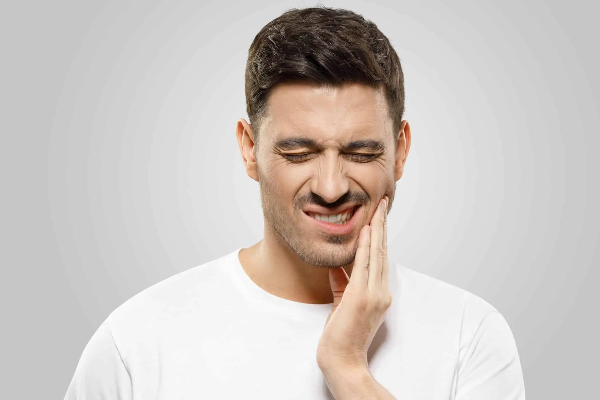 Ein Mann, der unter Zahnschmerzen leidet, hält schmerzerfüllt seine Hand und sucht Linderung durch osteopathische Techniken.