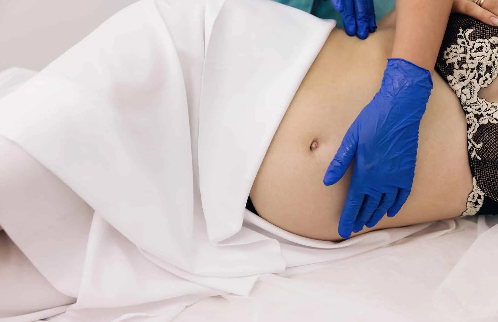 Eine schwangere Frau, die in Hamburg Kinderosteopathie erhält, liegt mit blauen Handschuhen bequem auf einem Bett.