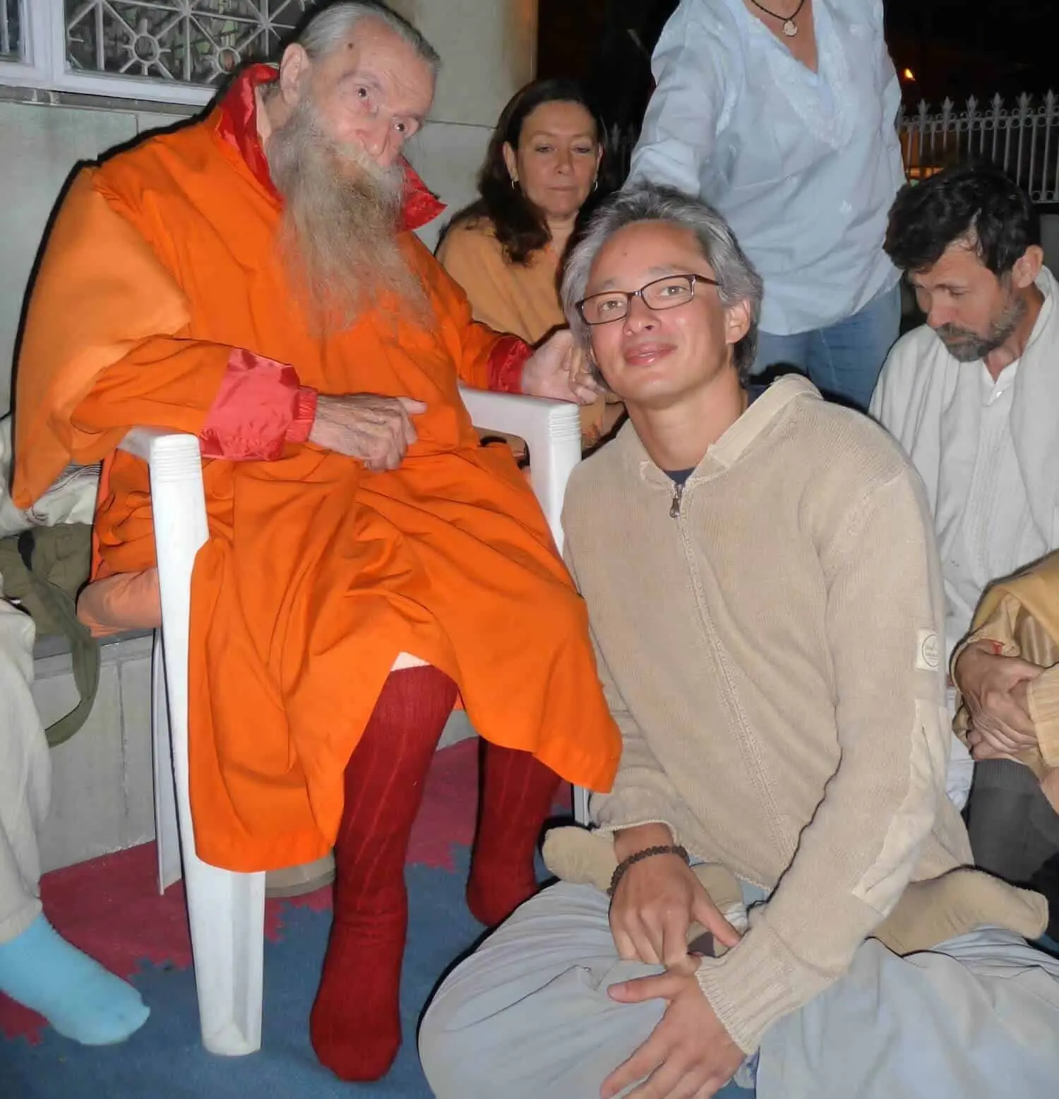 Eine Gruppe von Menschen sitzt während einer Kinderosteopathie-Sitzung um einen Mann in einem orangefarbenen Gewand.