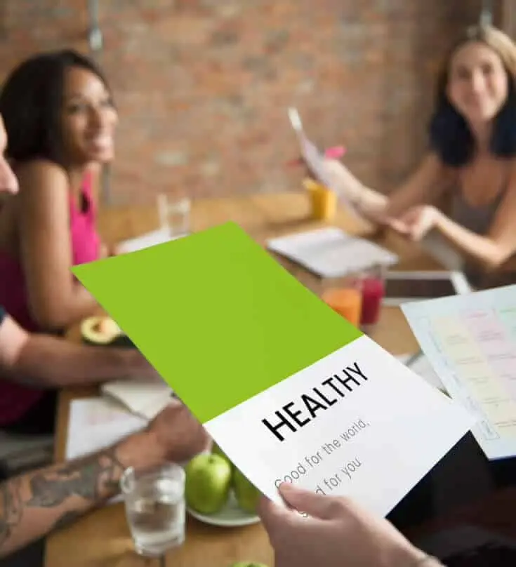 Eine Gruppe von Menschen sitzt an einem Tisch und hält ein grünes Papier mit dem Wort „gesund“.