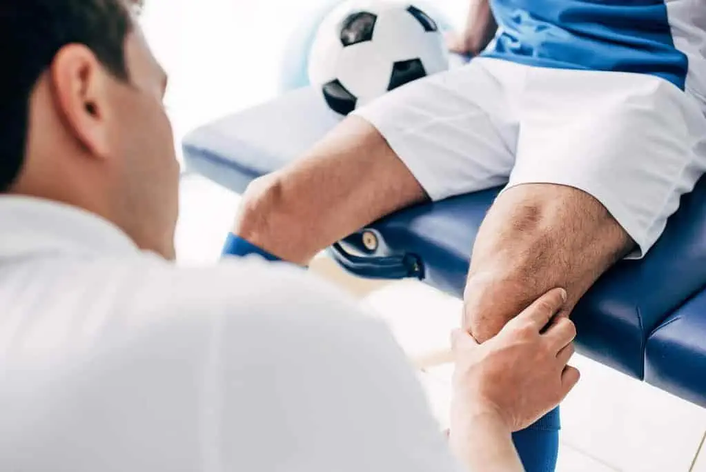 Ein Mann sitzt mit einem Fußball auf dem Knie auf einem Tisch und erhält Sportosteopathie.