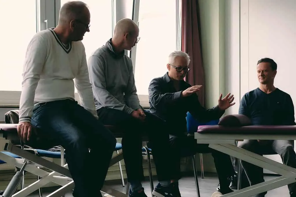 Eine Gruppe von Männern sitzt um einen Tisch in einem Raum und diskutiert über Sportosteopathie.