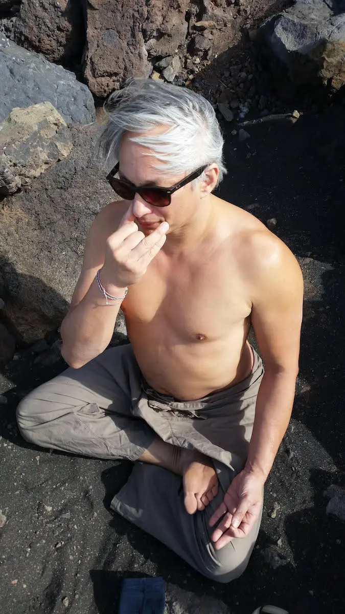 Ein Mann ohne Hemd, der auf einem Felsen sitzt und Sportosteopathie praktiziert.