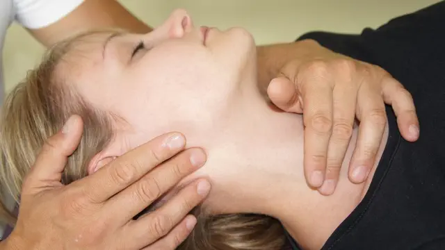 Eine Person, die in Rückenlage eine Nackenmassage erhält, genießt die osteopathischen Behandlungsansätze. Hände werden beidseitig auf den Nacken gelegt und üben sanften Druck aus. Mit geschlossenen Augen wirkt sie entspannt.